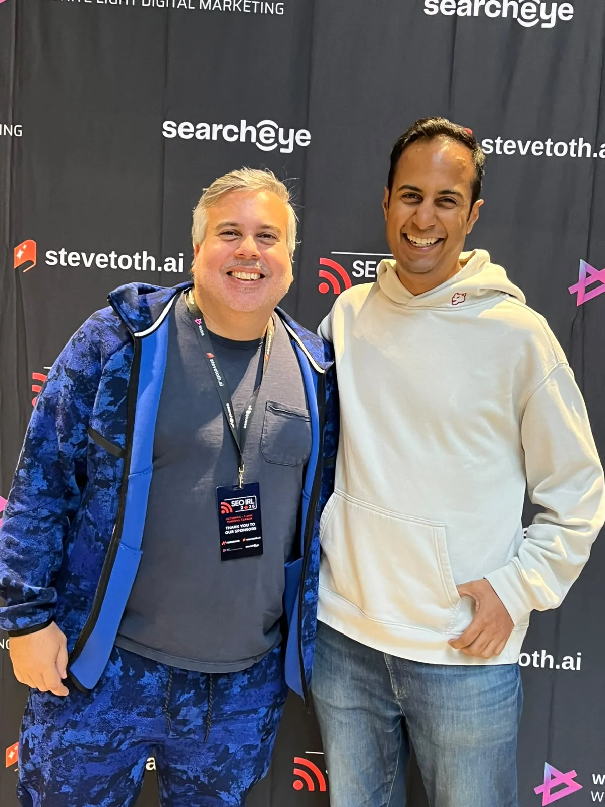 Two attendees smiling in front of the SEO IRL conference backdrop